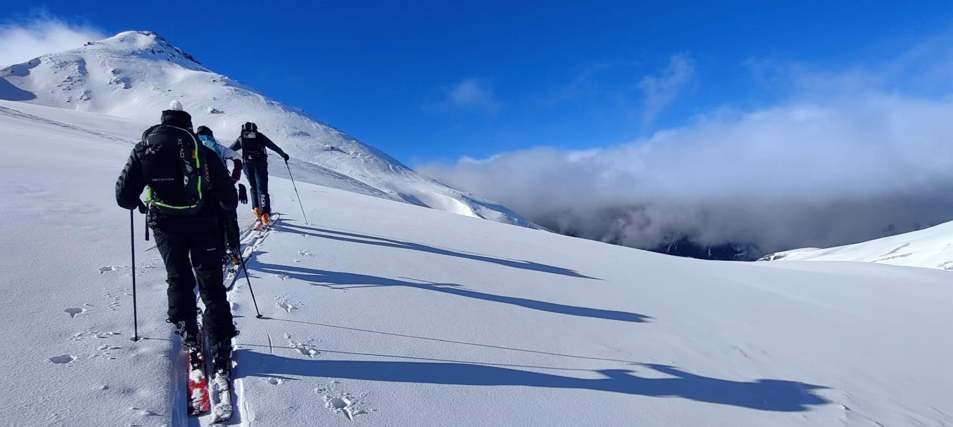 Skieurs de randonnée dans la neige poudreuse, ciel bleu et nuage de brouillard