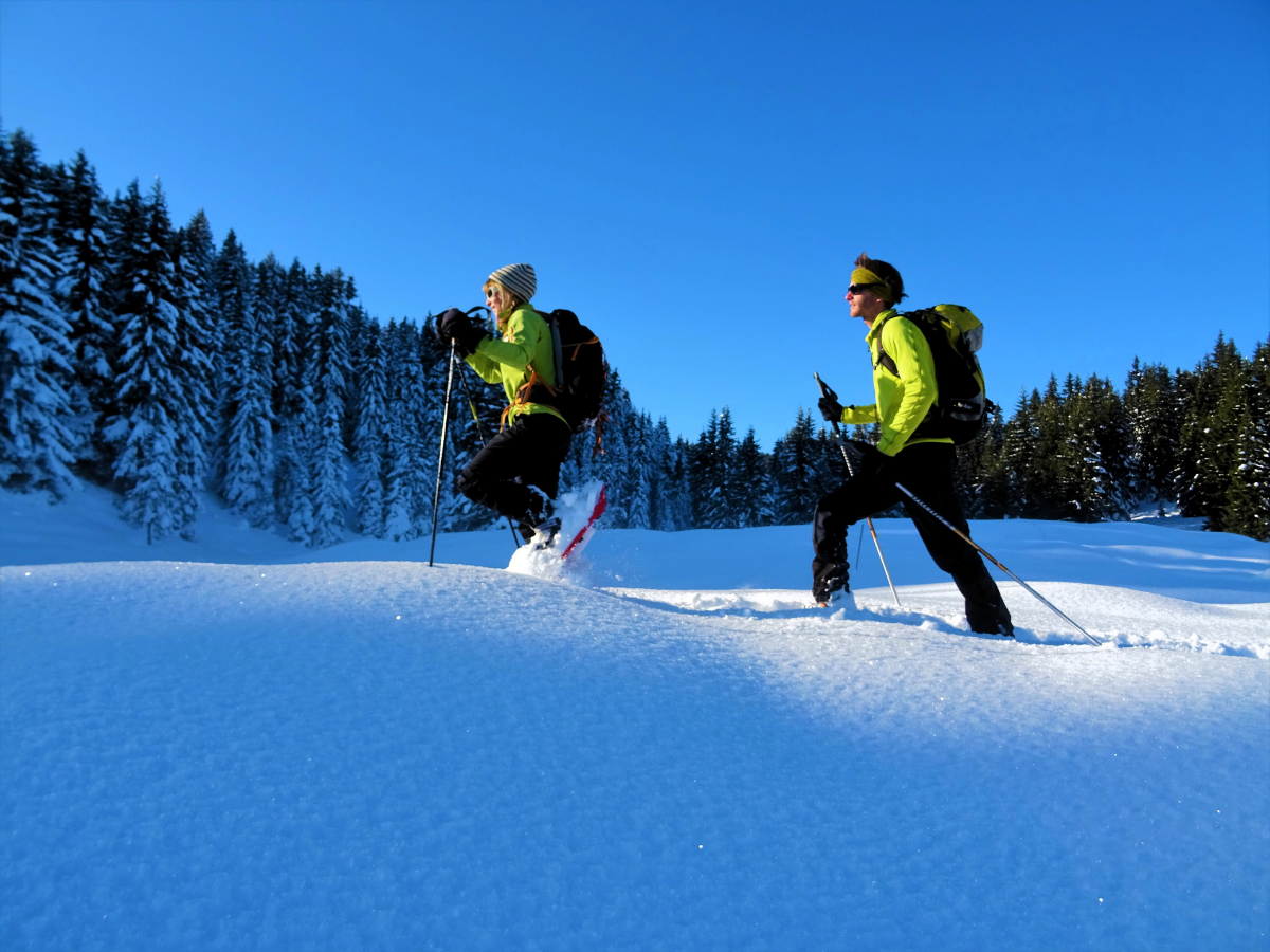 Deux randonneurs en raquettes progressent dans la neige profonde alors que le soleil se lève. Un belle journée s'annonce dans le Beaufortain