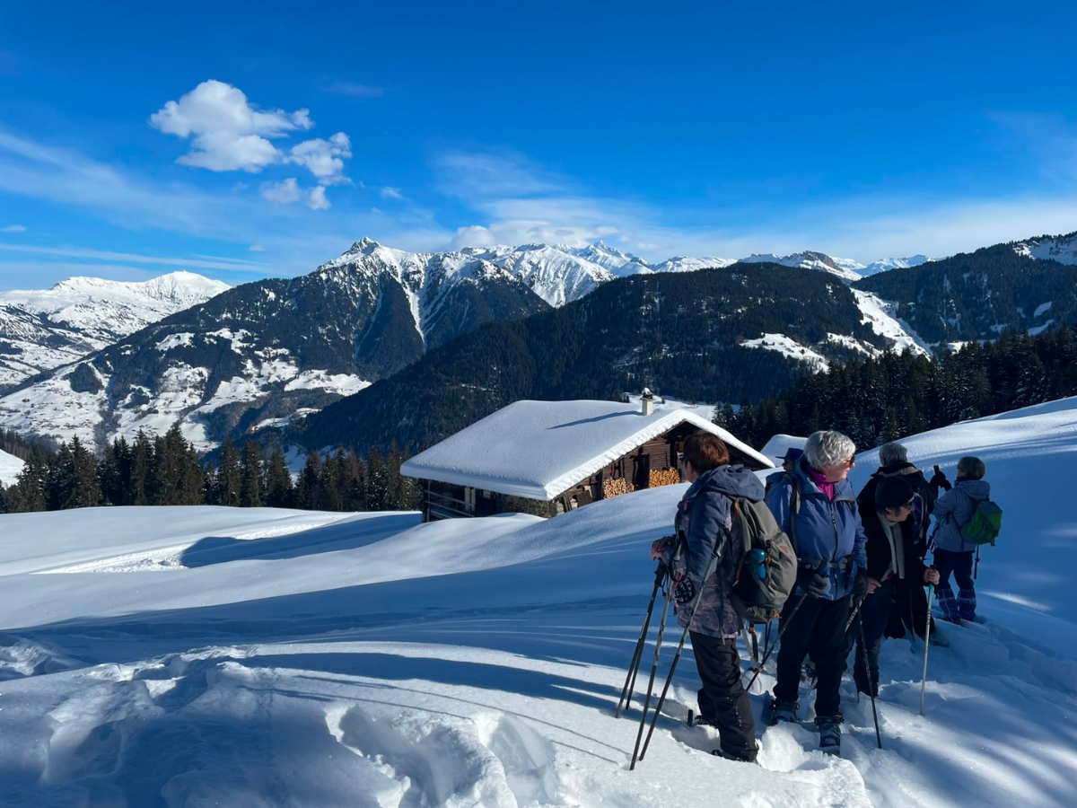 Un groupe de randonneurs à raquettes profite du paysage a proximité d'un chalet
