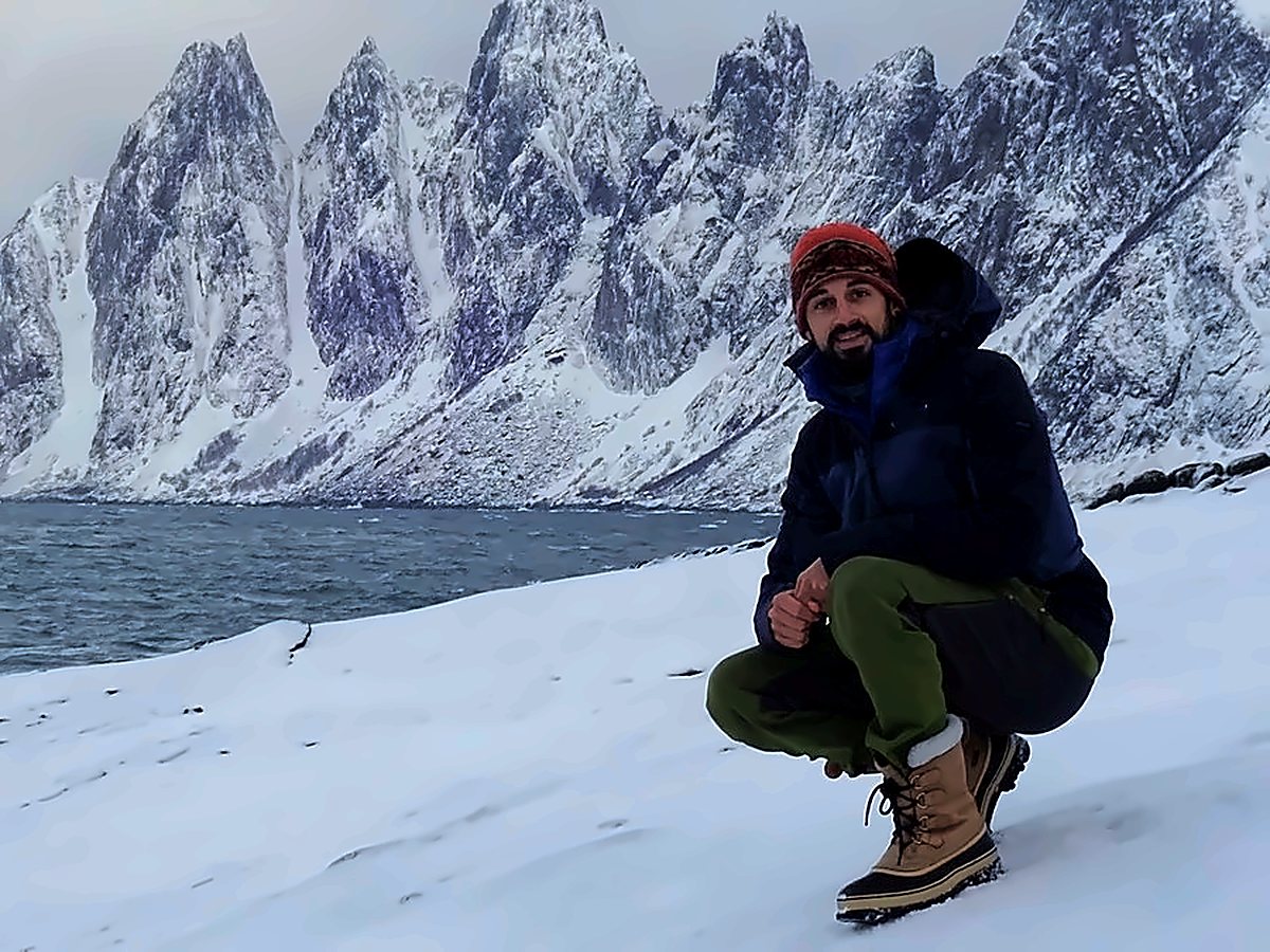 randonneur-neige-norvege©alvaro-ullivarri Randonneur accroupi dans la neige face aux pics enneigés d’Okshornan, au bord de la mer sur l’île de Senja en Norvège, sous un ciel d’hiver
