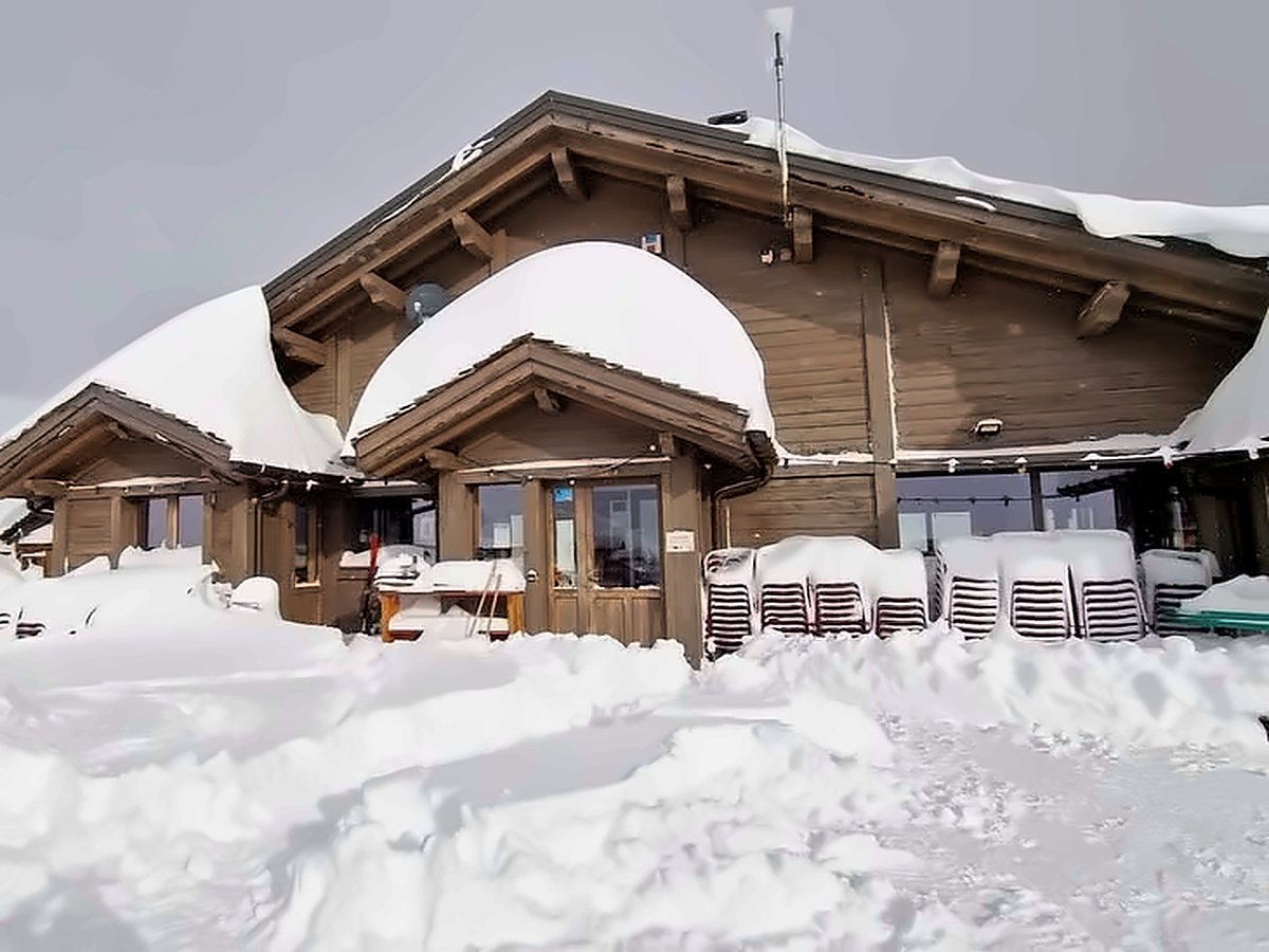 refuge-neige-areches©refuge-alpage Façade en bois du refuge ensevelie sous la neige fraîche, sur le domaine skiable d’Arêches Beaufort par temps grisRefuge d’altitude sous la neige au cœur du Beaufortain, face au Mont Blanc et aux sommets enneigés, sous un ciel bleu